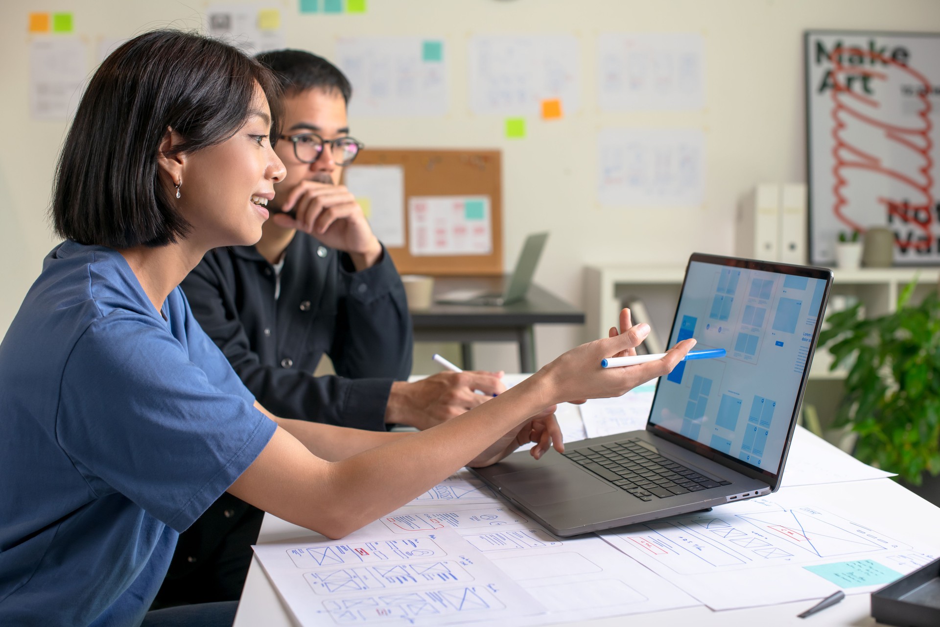 UX/UI designers discussing and brainstorming on wireframes for a website and mobile app prototype, surrounded by sketches of user flow and design tools, in the concept of website and mobile application design concept.